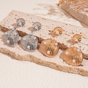 Detailed view of shell-shaped earrings with faux pearl drops in gold and silver finish