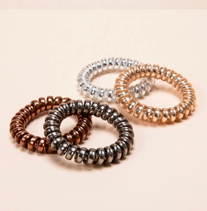 Detail of four metallic spiral hair ties in bronze, silver, and gold on a beige background