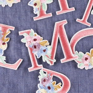 Pink floral embroidered letter patches with colorful flowers on blue denim fabric