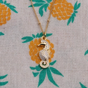 Gold seahorse pendant necklace with white enamel and sparkling zircon on pineapple background