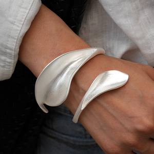 Macro shot of silver metal leaf open bangle with matte brushed texture on model wrist