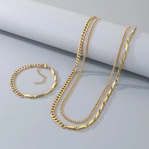 Detail of gold Cuban and bar link necklace and bracelet set on grey stone pedestal