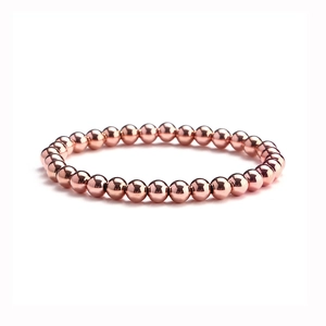 Detail of rose gold stainless steel beaded bracelet with elastic cord on white background