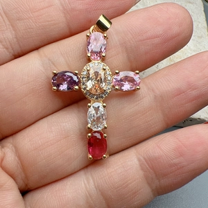 Detailed close-up of a gold cross pendant featuring colorful oval gemstones and zircon