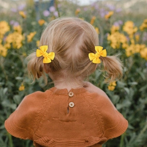 Toddler sweet yellow bow hair clips set on blonde pigtails in a field of flowers