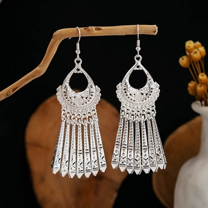 Close-up of silver boho ethnic earrings with hollow patterns and tassels on wood