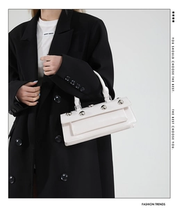 Detail of white leather baguette bag with silver rivets held by a model in a black suit