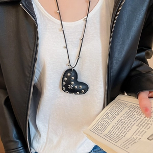 Detail of black leather heart pendant necklace with silver studs and cross on a model