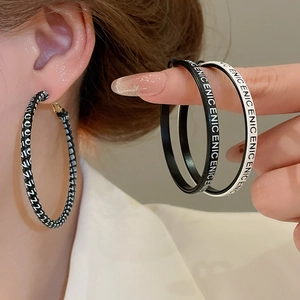 Gros plan de grandes créoles avec lettres ENIC en style cuir noir et blanc