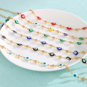 Detailed close-up of multi-colored enamel evil eye charms on golden beaded chain bracelets