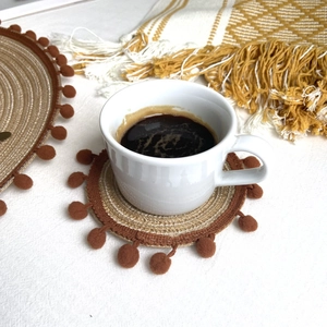 Detail of round woven coaster with brown pom pom fringe and beige cotton textures