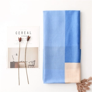 Flat lay of a blue and beige patchwork scarf with fringes next to a magazine