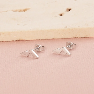 Gros plan détaillé de boucles d'oreilles sommets montagneux sur tissu rose