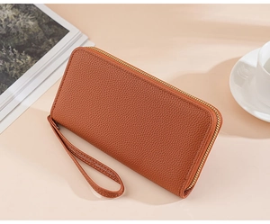 Brown litchi grain leather clutch wallet with gold zipper and wrist strap on beige surface