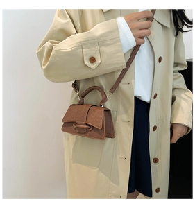 Mini sac bandoulière marron tressé porté par un mannequin en trench-coat beige