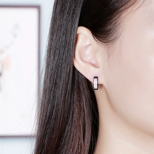Détail d'une boucle d'oreille noire sertie de deux rangées de strass blancs sur modèle