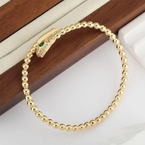 Golden snake-shaped beaded bracelet with green emerald eyes and zircon inlay jewelry