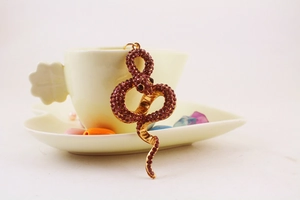 Detailed view of a gold snake keychain featuring sparkling deep pink rhinestones on a ceramic cup