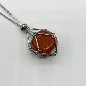 Macro shot of gold sandstone crystal pendant inside silver stainless steel mesh cage