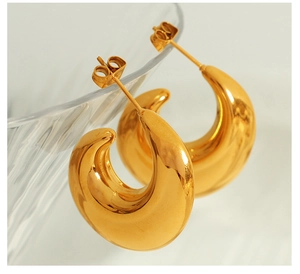Close-up of golden hollow crescent earrings with mirror finish on glass vessel