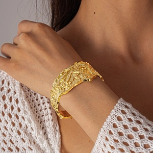 Macro shot of chunky gold open cuff bracelet with lava texture on woman's wrist