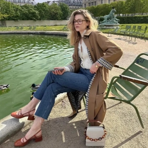 Khakifarbener Trenchcoat kombiniert mit weißem Spitzentop und blauer Jeanshose
