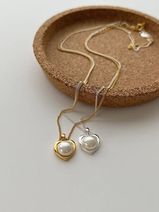 Dettaglio di collane a cuore in oro e argento con perle su vassoio in sughero