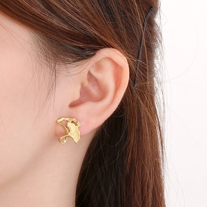 Macro shot of gold ginkgo leaf stud earring showing brushed metal texture on ear