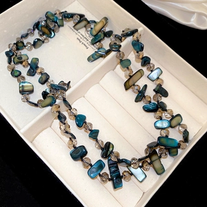 Close-up of irregular abalone shell fragments and faceted crystal beads on a necklace