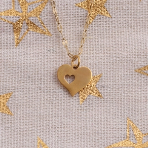 Macro detail of gold heart pendant necklace with cutout design on textured fabric