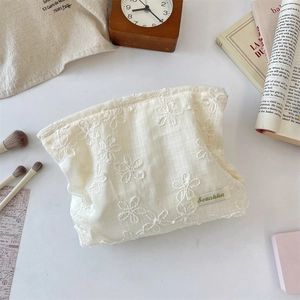 Detail of cream lace cosmetic bag with 3D floral embroidery and side brand tag