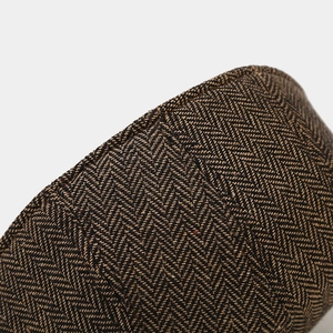 Close-up of brown herringbone fabric texture on the newsboy cap with neat stitching