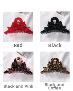 Detail of four acetate bow hair clips in red, black, and tortoiseshell on white fabric