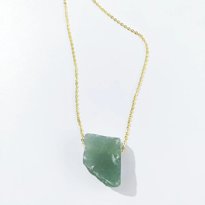 Detailed view of the irregular green crystal pendant on a thin golden necklace chain