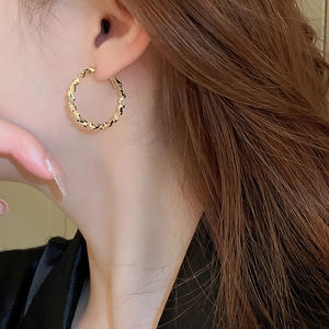 Close-up of golden irregular hoop earring with twisted texture on female model's ear