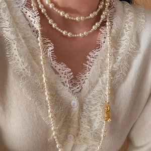 Detail view of multilayer pearl necklace with gold clasp on a lace sweater