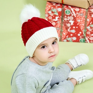 Close-up of child wearing red knit Christmas hat with white pompom and gift box