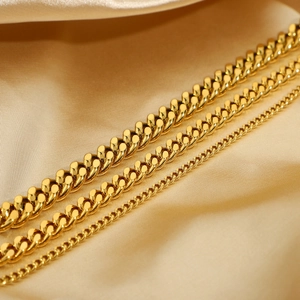 Three gold Cuban link anklets in varied widths displayed on luxury silk fabric
