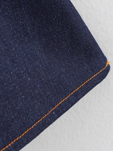 Detail macro shot of dark blue denim fabric with orange stitching and twill texture