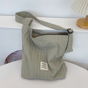 Detail of green pleated tote bag with adjustable black buckle strap on a minimalist desk