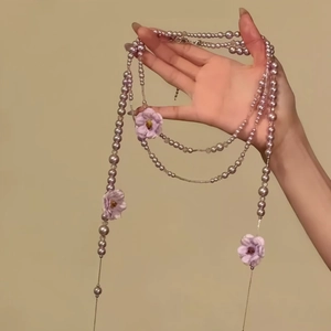 Detailansicht der langen lila Perlenkette mit Stoffblumen an der Hand drapiert