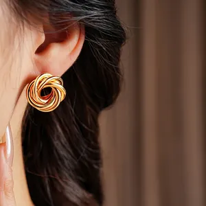Polished gold geometric twisted hoop earrings worn by a model in a close-up shot