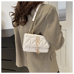 Close-up of white quilted square bag with gold chain strap and tassel on brown suit
