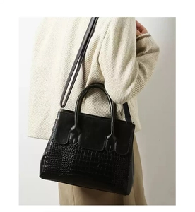 Detail of black faux leather handbag with crocodile pattern texture and top handle