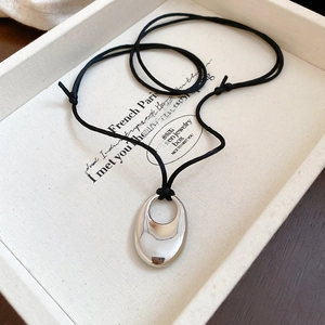 Détail d'un pendentif ovale en métal argenté sur un cordon noir dans un écrin