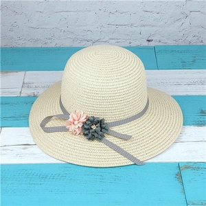 Detail of a beige straw sun hat featuring floral accents and a polka dot ribbon bow