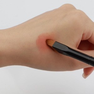 Detailed view of the flat concealer brush applying makeup on the hand with precision
