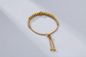 Detailed view of golden bead bracelet with adjustable slide clasp on textured background