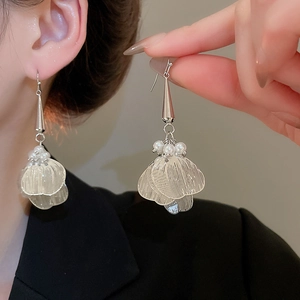 Detail view of hollow petal pearl tassel earrings with silver cone caps worn by a model