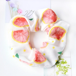 Close-up of a white fabric scrunchie with pink grapefruit slices and green leaf patterns